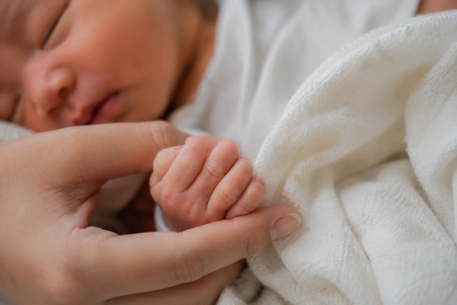 Bàn tay người lớn nâng bàn tay của trẻ sơ sinh đang ngủ